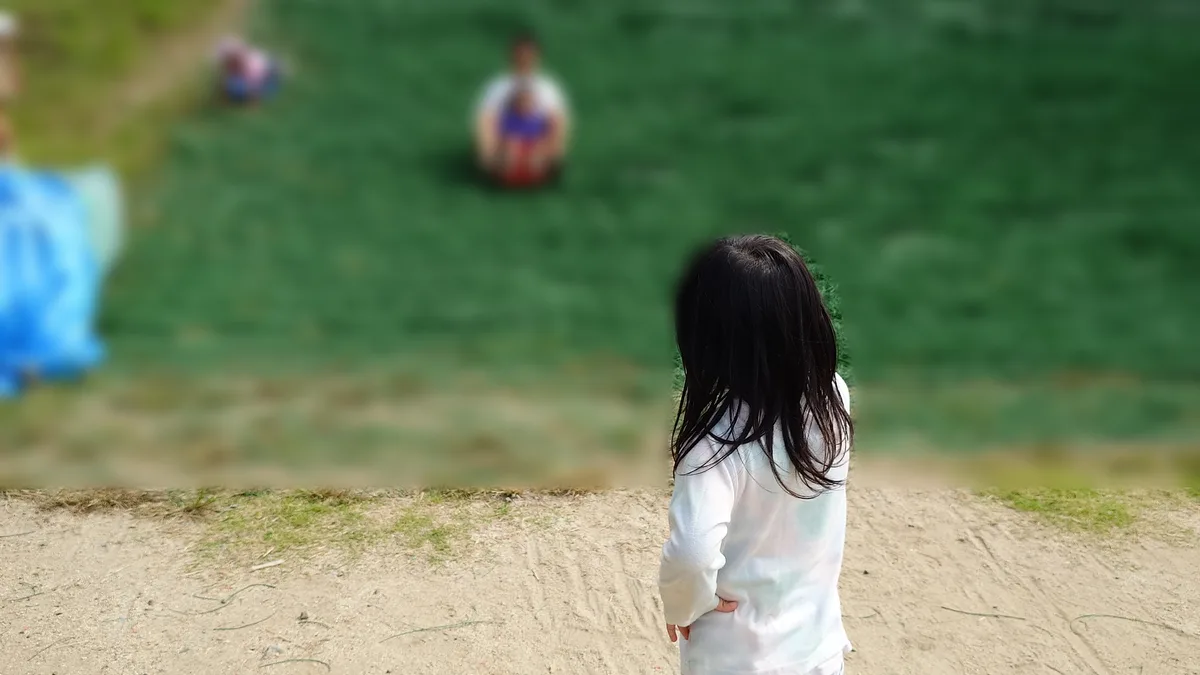 人工芝すべりの坂の下で、すべる人を見上げる4歳の後ろ姿